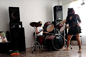 they play the drums for her - she dances stripping and showing her ass